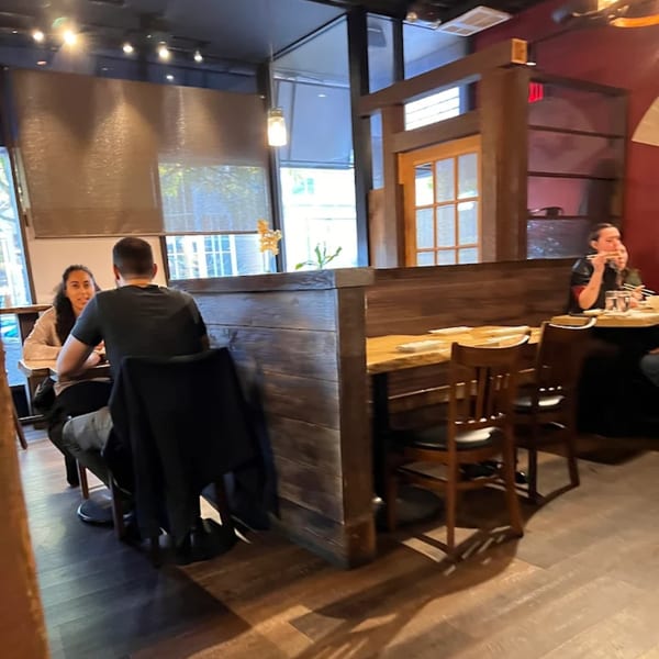 Diners seated at wooden tables with booth seating and chairs inside KANBU Sushi Downtown.