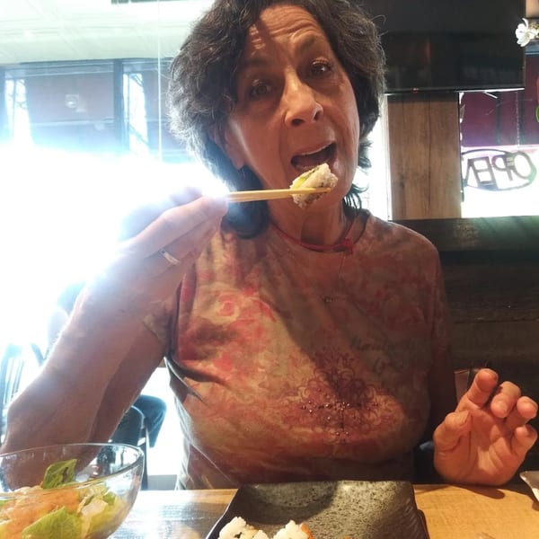 A woman at KANBU Sushi Downtown is about to eat a piece of sushi with chopsticks.