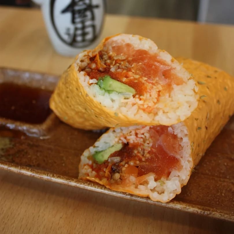 A KANBU Sushi burrito, cut in half, revealing salmon, rice, and avocado, on a brown plate.