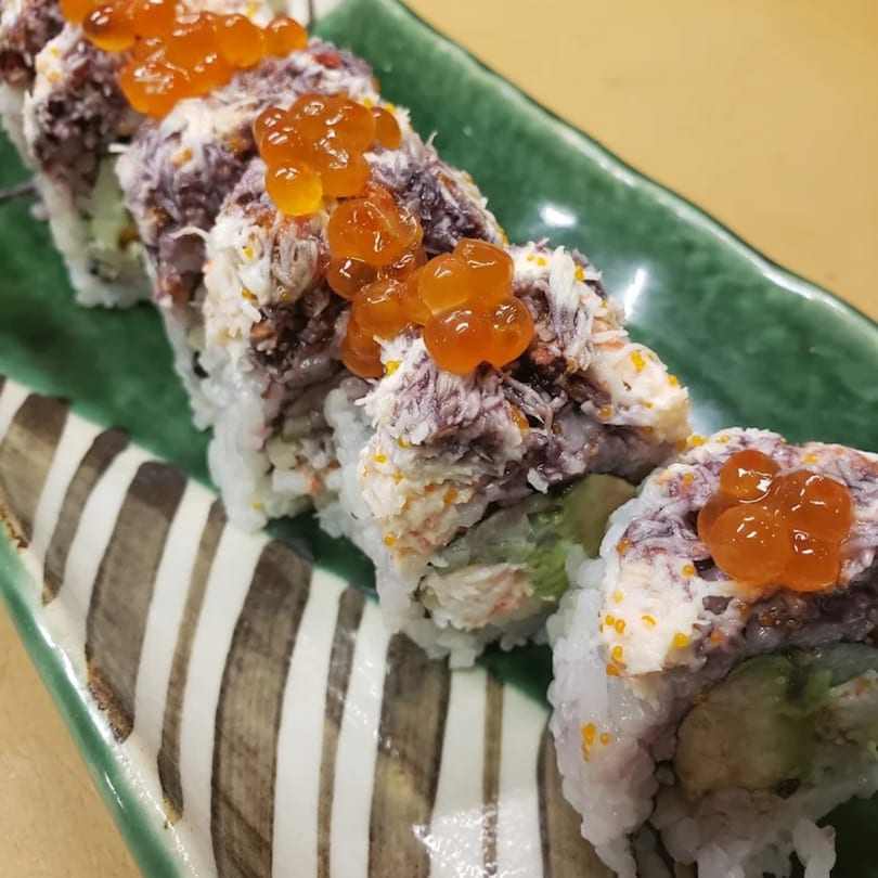 KANBU Sushi Downtown's sushi roll with crab, avocado, and bright orange roe on a green and white striped plate.