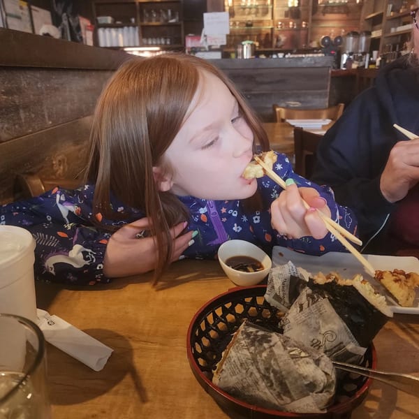 A young girl in a unicorn jacket eats sushi with chopsticks at KANBU Sushi Downtown.