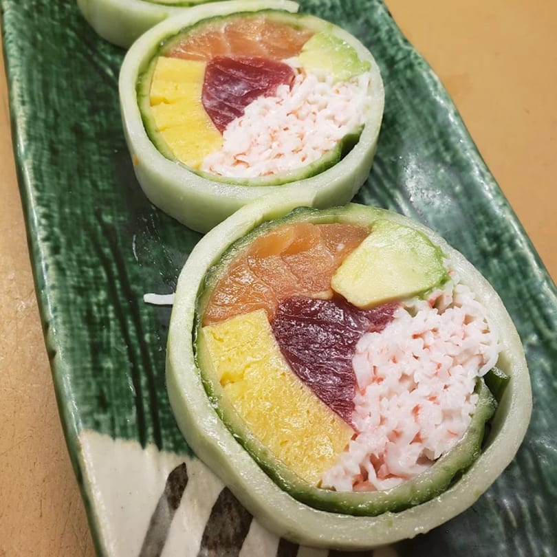 Two vibrant KANBU Sushi rolls with salmon, tuna, avocado, egg, and crab on a green plate.