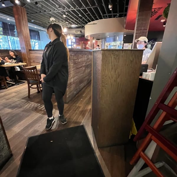 A server stands in the KANBU Sushi Downtown dining area with customers seated at tables.