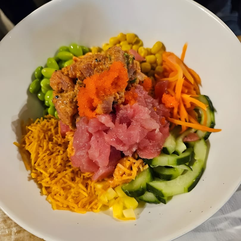 A colorful KANBU Sushi poke bowl with tuna, edamame, corn, carrots, cucumbers, and crispy toppings.