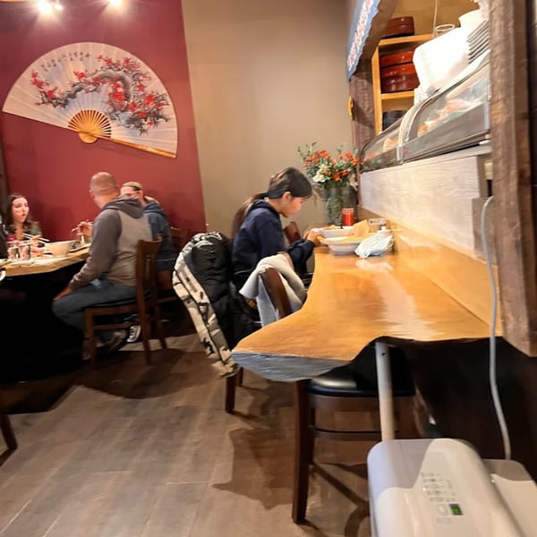Diners enjoying sushi at KANBU Sushi Downtown, with a large decorative fan on the red wall.